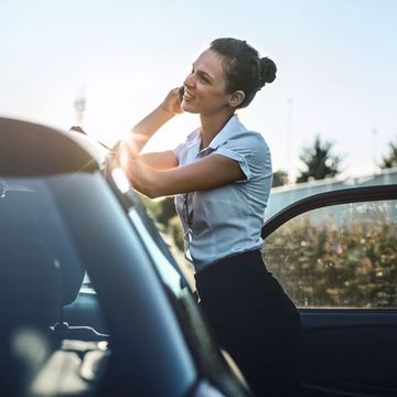 Mujer joven conversa al teléfono junto a su coche de renting