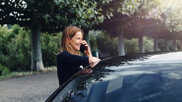 Woman on phone leaning on car 