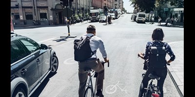 Two people on bikes next to car