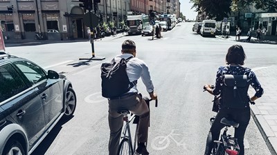 Two people on bikes next to car