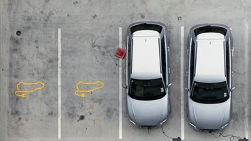 Två silvriga EV elbilar laddar batterierna bredvid varandra på en parkeringsplats 